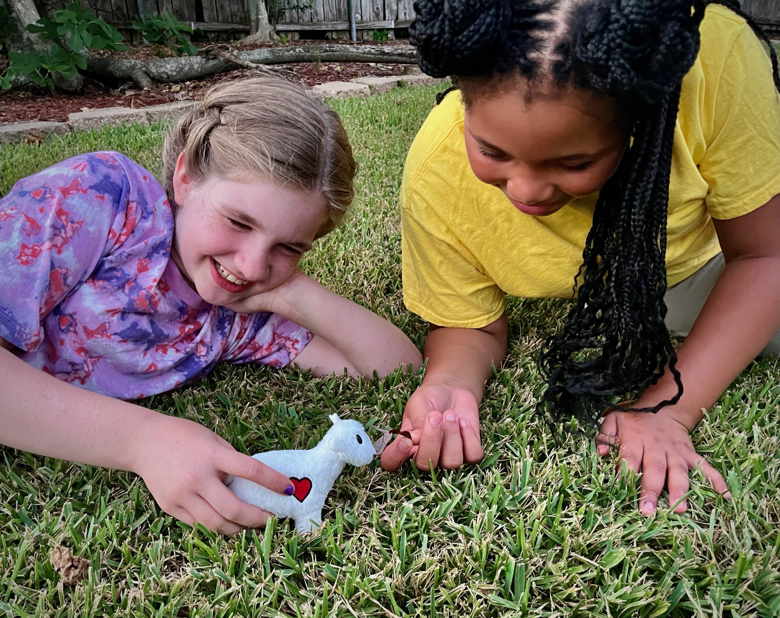 Two girls play with a stuffed lamb.